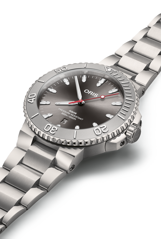The Oris Aquis Date Relief wristwatch features a metal band, grey dial, date window, and bold white hour markers.