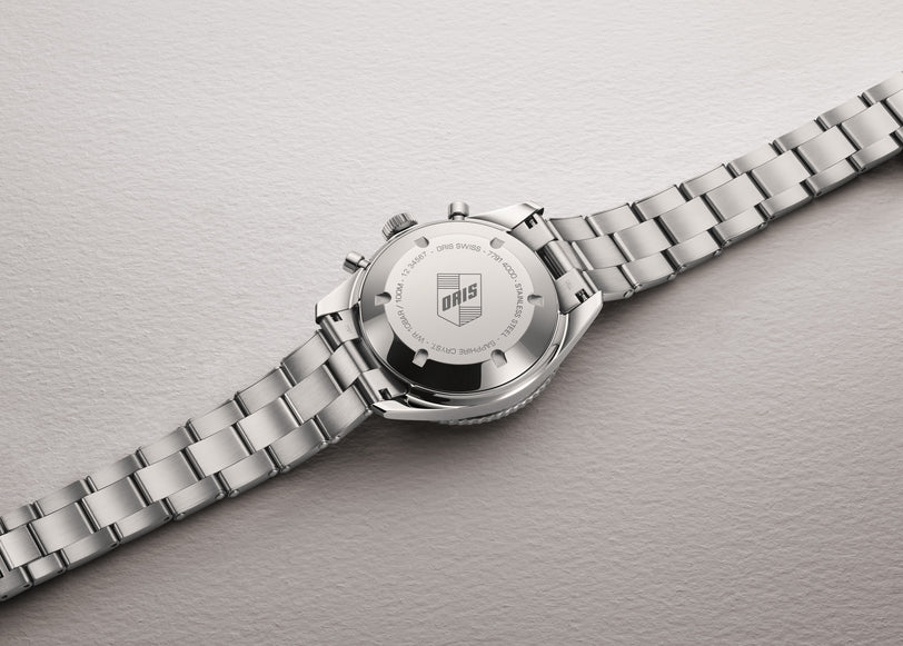 Back of the Oris Divers Sixty-Five Chronograph silver wristwatch with engraved logo and text, displayed on a light textured surface.