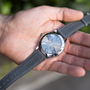 A person holds a Chopard L.U.C XPS 1860 Officer Limited Edition For Hodinkee, showing its intricate swirling guilloché back and grey leather strap.