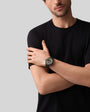 A man in a black t-shirt crosses his arms, showcasing the Zenith Defy Extreme Diver wristwatch in black and yellow against a plain background.