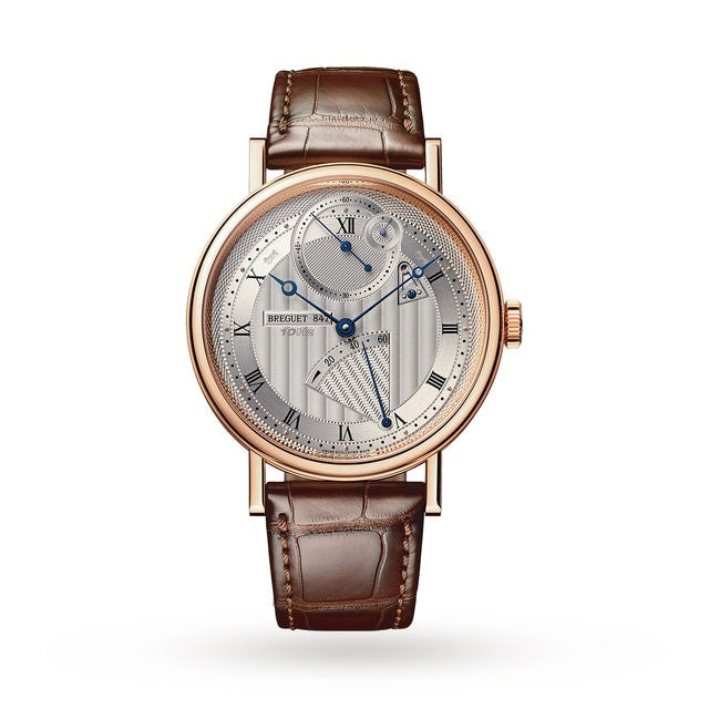 The Breguet Classique Chronométrie 7727 is a luxury wristwatch with a brown leather strap, rose gold round case, silver textured dial, blue hands, Roman numerals, and a small seconds subdial.