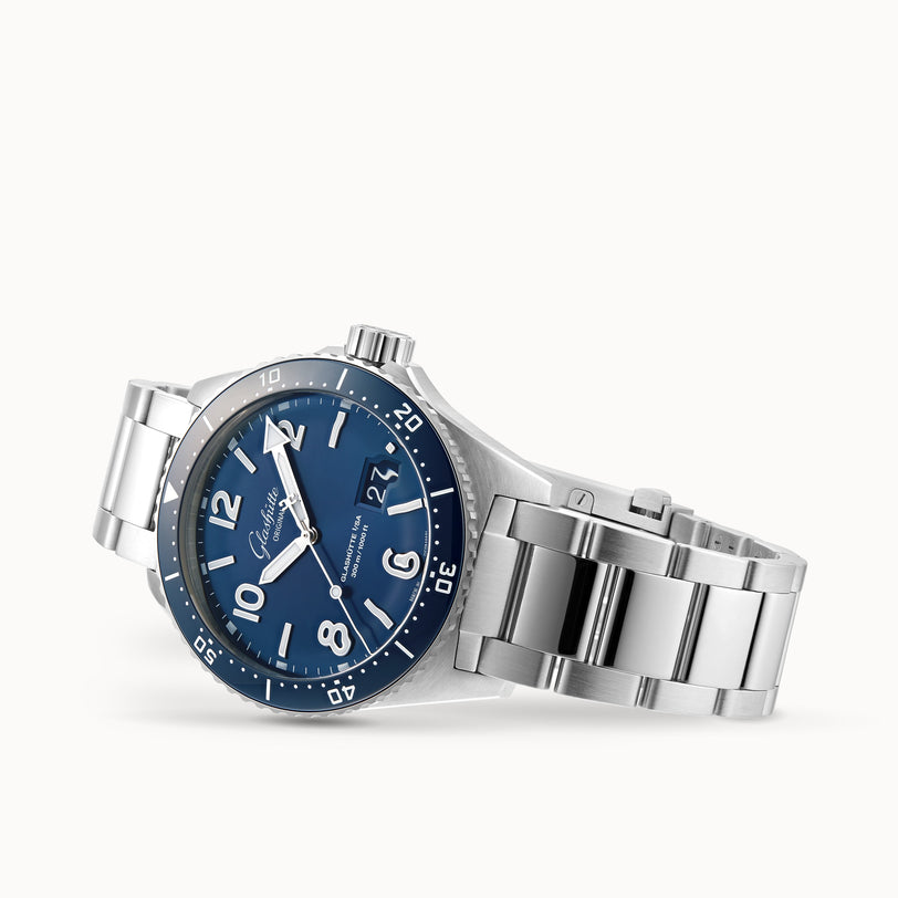 The Glashütte Original SeaQ Panorama Date, a stainless steel watch with a blue dial, white markers, date display, rotating bezel, and metal bracelet, is shown on its side for visual appeal.