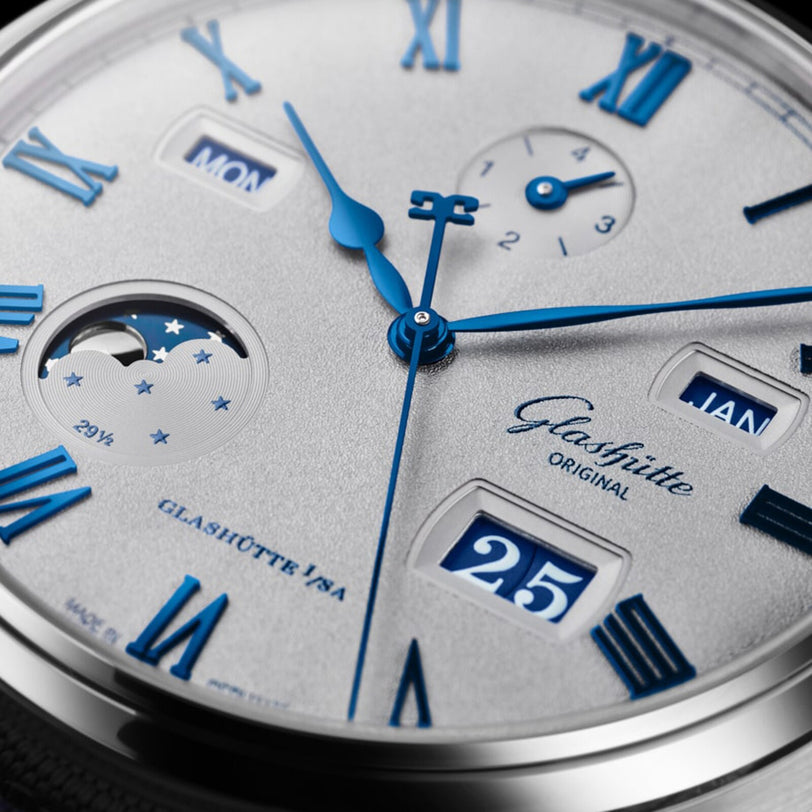 Close-up of the Glashütte Original Senator Excellence Perpetual Calendar watch face, featuring blue Roman numerals, moon phase, and date windows.