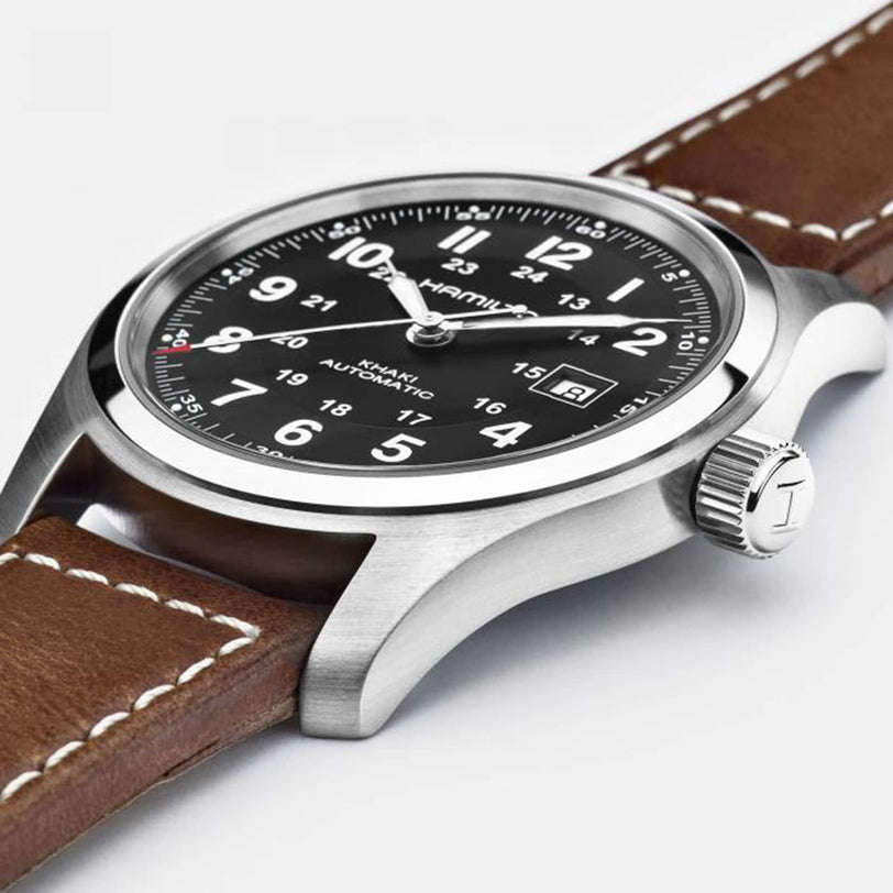 A close-up of the Hamilton Khaki Field Auto wristwatch featuring a black dial with white numerals, date display, brown leather strap with white stitching, and the H-10 automatic caliber for an extended power reserve.