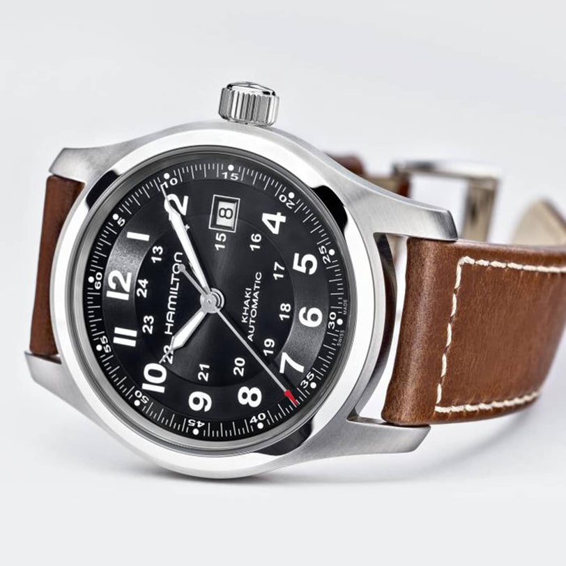 The Hamilton Khaki Field Auto is a stainless steel watch with a black dial, white numerals, date display, brown leather strap, and H-10 automatic caliber for extended power reserve, shown against a plain background.