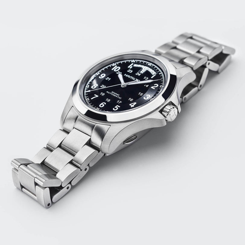 The Hamilton Khaki Field King Auto showcases a stainless steel case, black dial with military time, white numerals, and a metal link band, displayed against a light background.
