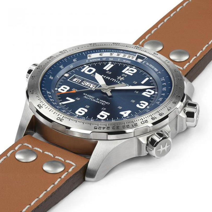 The Hamilton Khaki Aviation X-Wind Day Date Auto is a silver analog watch with a blue dial, SuperLumiNova® numerals, brown leather strap, three crowns, and an automatic day-date display.