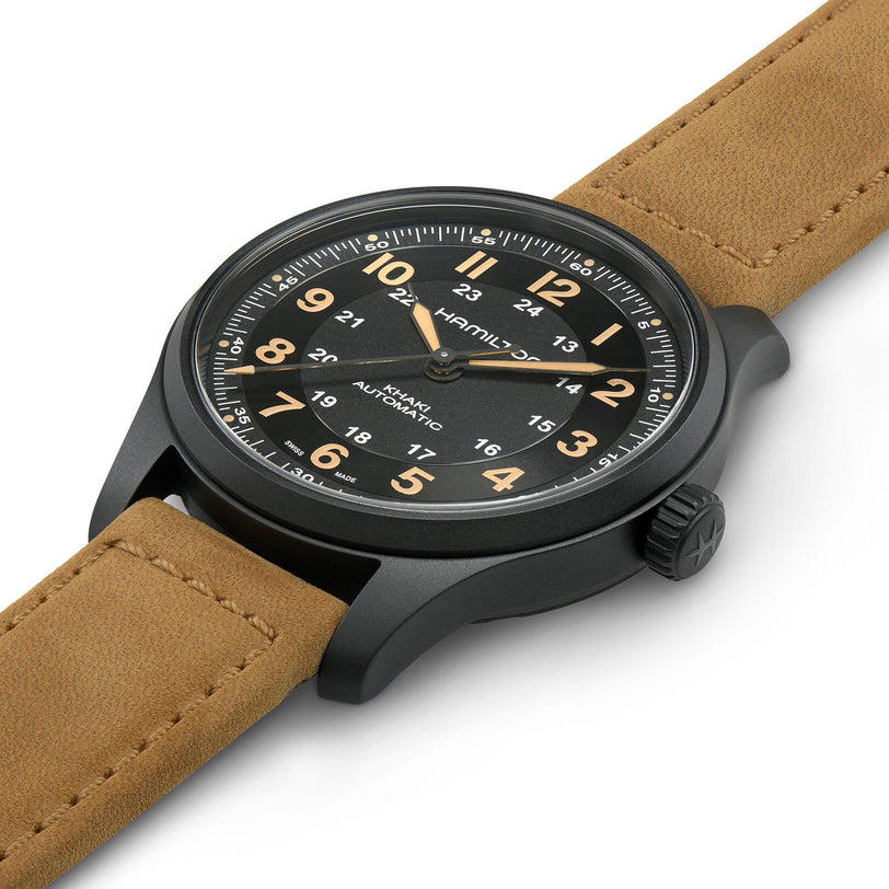 The Hamilton Khaki Field Titanium Auto is a black wristwatch with a brown leather strap, military-inspired design, black dial, Arabic numerals, and white and orange details, shown angled on a white background.