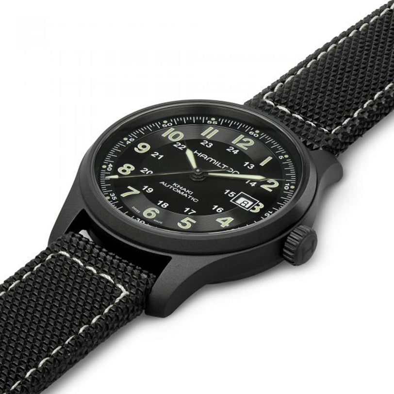 The Hamilton Khaki Field Titanium Auto is a mens black watch with a fabric strap, white stitching, black dial, white numerals, luminous hands, and a date window at 3 oclock.