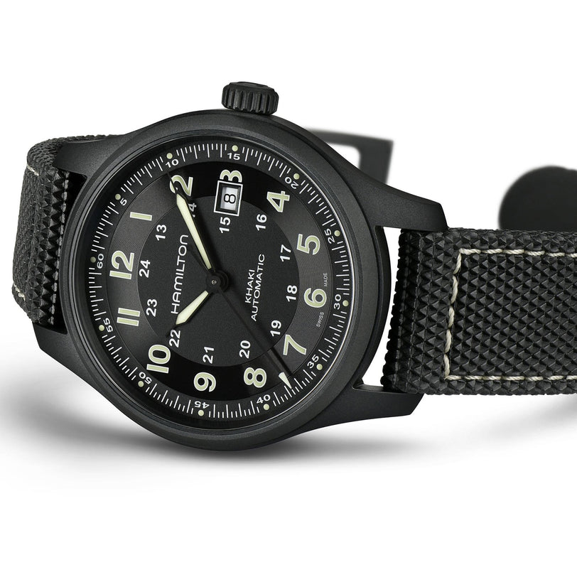 The Hamilton Khaki Field Titanium Auto is a men’s watch with a black case, textured strap, white numerals, and a date display at 3 o’clock.