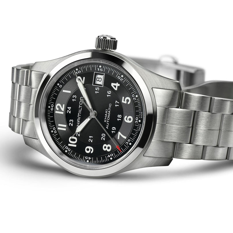 The Hamilton Khaki Field Auto, a stainless steel watch with black dial, silver markers, and 12/24-hour markings, is shown at an angle on a metal bracelet, reflecting refined military-inspired style and automatic movement.