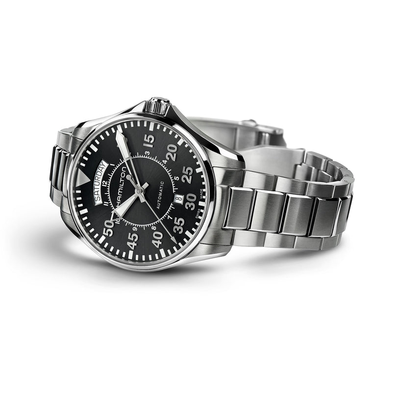 The Hamilton Khaki Aviation Pilot Day Date Auto is a stainless steel aviator wristwatch featuring a black dial with white numerals, day and date display, automatic movement, and a metal bracelet, shown angled slightly to the right.