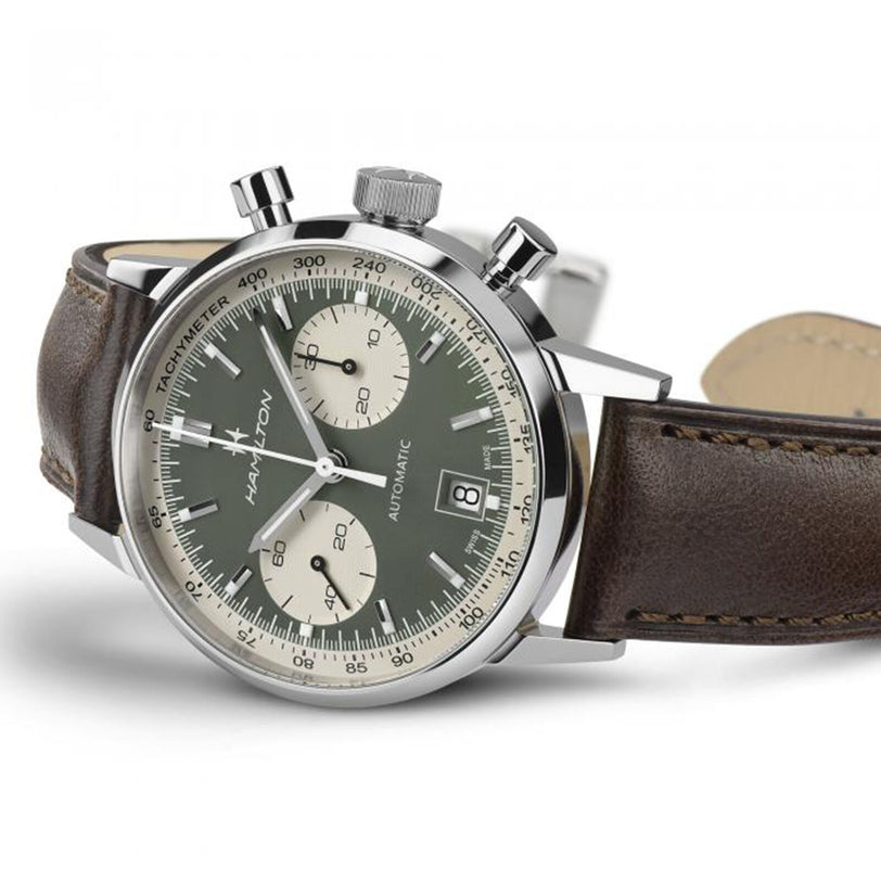 The Hamilton American Classic Intra-Matic Auto Chrono 40mm showcases vintage style with a green panda dial, two white subdials, date window, silver case, and brown leather strap, displayed at an angle.
