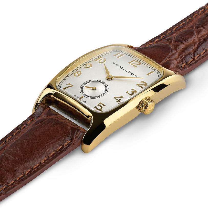 The Hamilton American Classic Boulton Quartz features a gold-tone rectangular case, brown leather strap, Arabic numerals, and a small seconds subdial at 6 o’clock—an elegant Swiss-made timepiece.