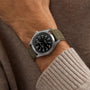 A person wearing the Hamilton Khaki Field Titanium Auto watch with a khaki fabric strap and black dial, styled over a beige knit sweater.