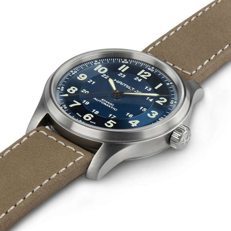 The Hamilton Khaki Field Titanium Auto, featuring a blue dial with beige Arabic numerals and a tan leather strap, is angled on a white background—an all-purpose stainless steel-look military watch.