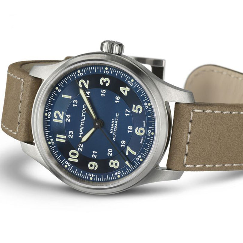 The Hamilton Khaki Field Titanium Auto is an all-purpose watch featuring a blue dial, silver case, tan leather strap, and 12/24-hour markers—drawing inspiration from classic Hamilton military designs.