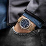 A person, seen from the waist up with one hand in a jeans pocket, wears a Hamilton Khaki Field Titanium Auto watch featuring a blue dial and brown leather strap.