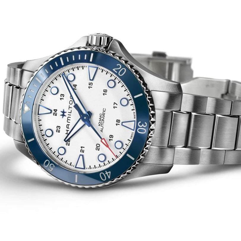The Hamilton Khaki Navy Scuba Auto features a stainless steel case, blue ceramic bezel, white dial, and silver markers—shown on its side with a partially open bracelet. Ideal for summer adventures at sea.