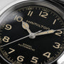 Close-up of the Hamilton Khaki Field Murph 38mm watch face with beige numerals, sword-shaped hands, and minute markers on black, powered by an automatic movement offering an 80-hour power reserve.
