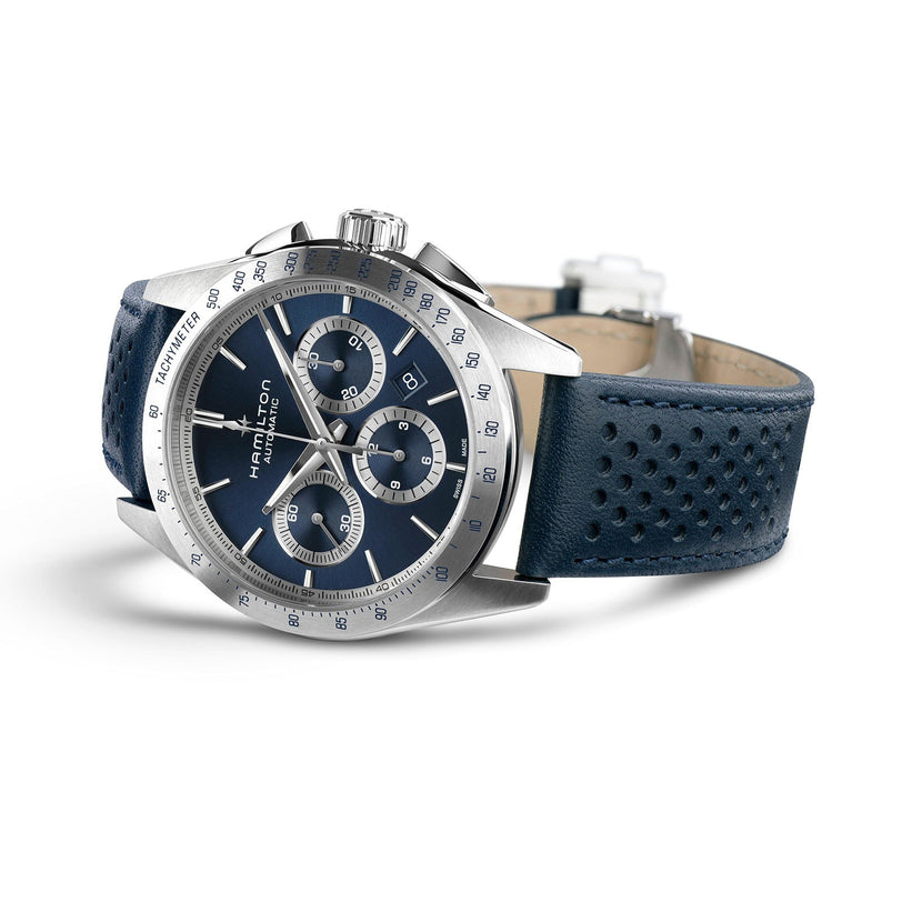 The Hamilton Jazzmaster Performer Auto Chrono features a stainless steel case, blue dial with chronograph subdials, tachymeter bezel, and a perforated blue leather strap, highlighting its craftsmanship against a white background.