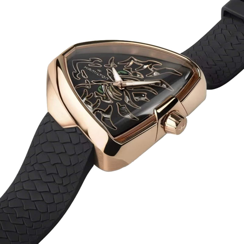 The Hamilton Khaki Field King Auto is a gold triangular wristwatch with a black patterned strap and an intricate skeleton dial.