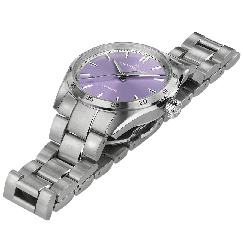 The Hamilton Jazzmaster Performer Auto wristwatch features a stainless steel case, metallic bracelet, and purple dial with automatic movement, shown against a white background.