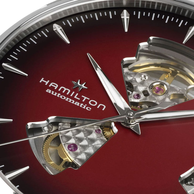 Close-up of the Hamilton Jazzmaster Open Heart Auto watch featuring a red dial, silver hands, exposed gears, and visible jewel bearings.