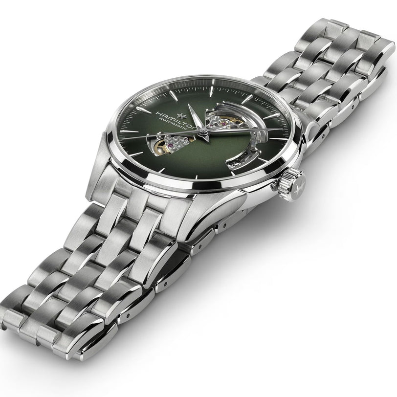 The Hamilton Jazzmaster Open Heart Auto 42mm is a silver wristwatch with a green dial, metal link band, and an exposed gear mechanism.