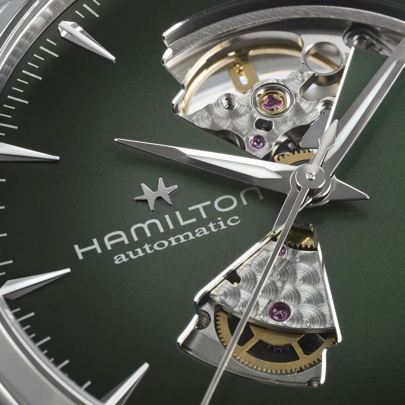Close-up of the Hamilton Jazzmaster Open Heart Auto 42mm watch face, showcasing exposed gears against a green metallic background.