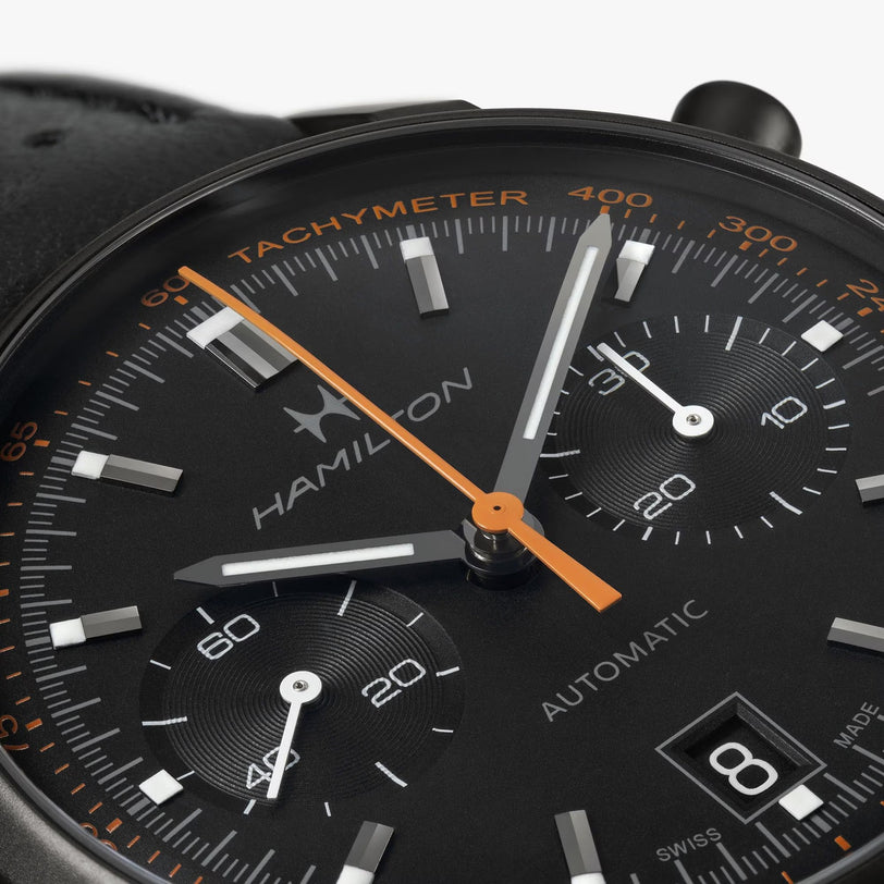 Close-up of a Hamilton American Classic Intra-Matic Auto Chrono watch in black with orange and white accents, featuring a date display at 4 o’clock.