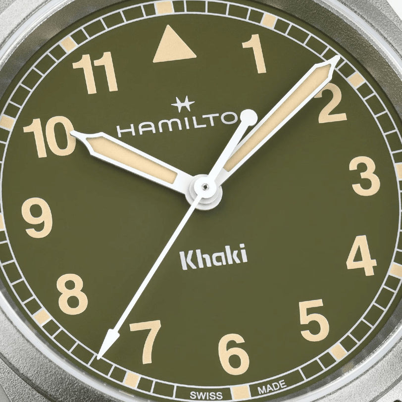 Close-up of the Hamilton Khaki Field Quartz 33mm watch face with white hands, beige indices, Arabic numerals, and a green background—highlighting its military heritage. The time shown is about 10:10:36.