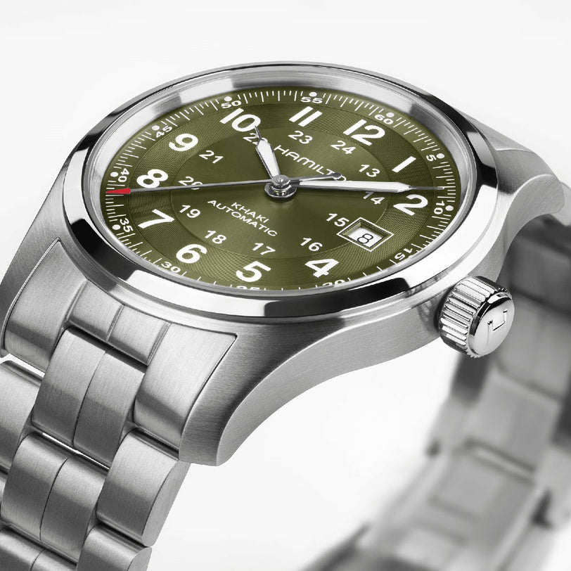 The Hamilton Khaki Field Auto 42mm features a stainless steel case, olive green dial with white Arabic numerals, date at 3 o’clock, silver metal bracelet, and H-10 automatic movement inspired by military heritage.