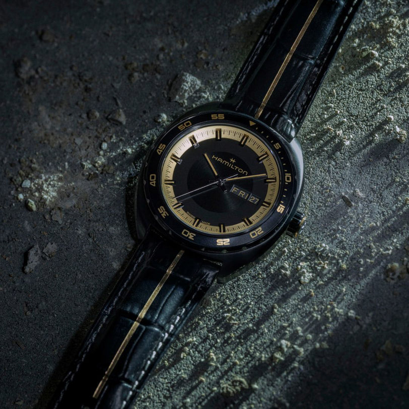 Luxury watch with black leather strap and gold accents on a textured dark surface