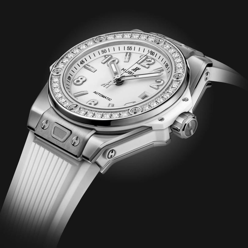 A Hublot Big Bang One Click Steel White Diamonds wristwatch with a white face, self-winding movement, diamond bezel, and white strap is elegantly displayed on a black background.