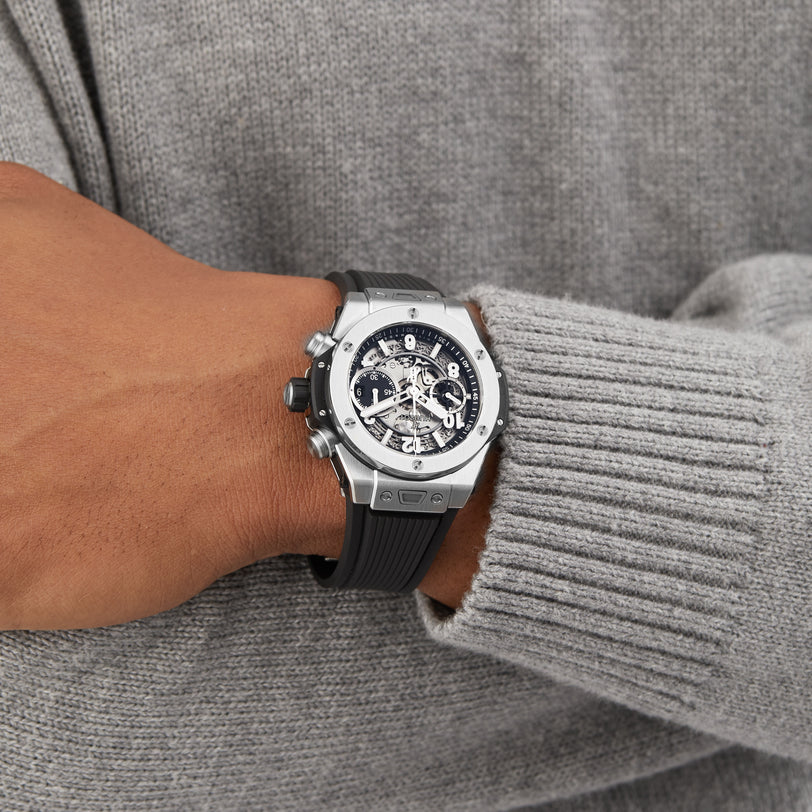 A person wearing a Hublot Big Bang Unico Titanium wristwatch with a visible chronograph flyback movement, dressed in a gray ribbed sweater.