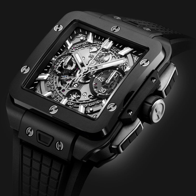 A close-up of the Hublot Square Bang Unico Black Magic wristwatch, showcasing its sapphire crystal skeleton dial, visible gears, chronograph functions, and textured rubber strap.
