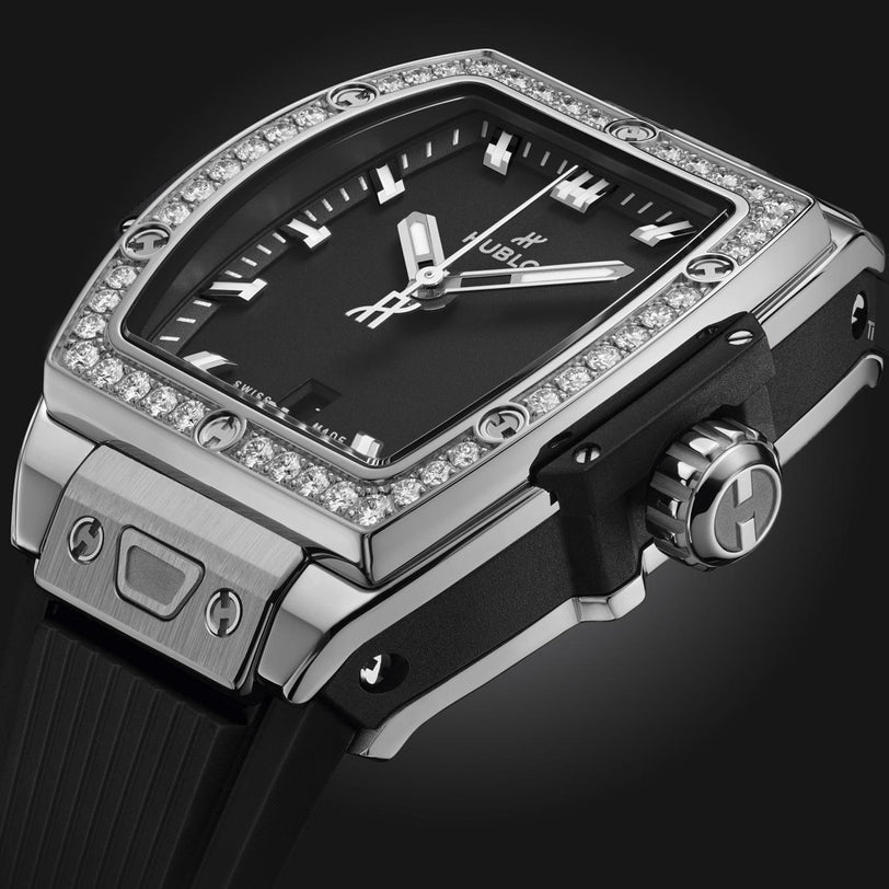 A close-up of the Hublot Spirit Of Big Bang Steel Diamonds wristwatch, featuring a black face, diamond-studded bezel, silver accents, and a black rubber strap against a dark background.
