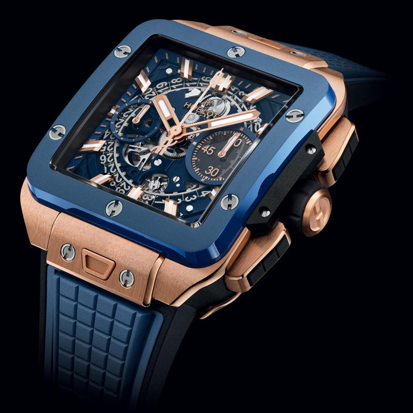 A close-up of the Hublot Square Bang Unico King Gold Blue Ceramic, featuring a blue bezel, King Gold case, open gears, blue rubber strap, and chronograph flyback function.