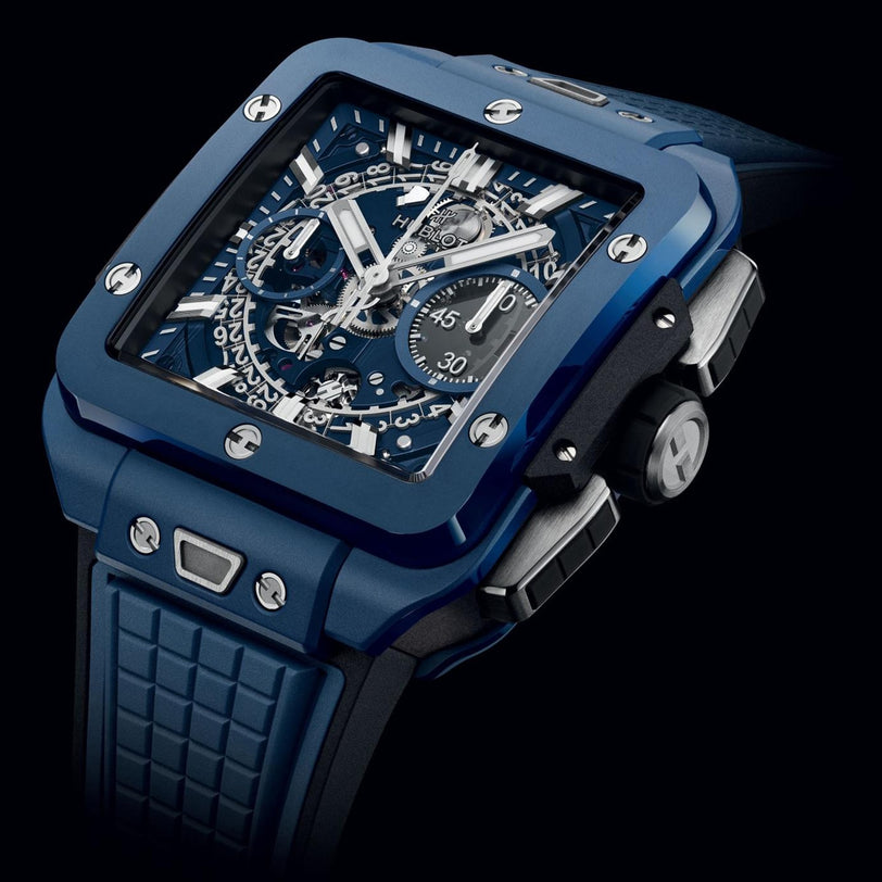 The Hublot Square Bang Unico Blue Ceramic is a luxury wristwatch with a sapphire crystal dial, skeleton display showing the HUB1280 UNICO movement, chronograph subdials, and a textured rubber strap.
