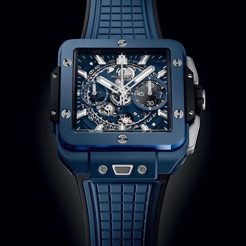 The Hublot Square Bang Unico Blue Ceramic wristwatch features an exposed mechanical dial with chronograph subdials and a textured rubber strap, displayed against a black background.