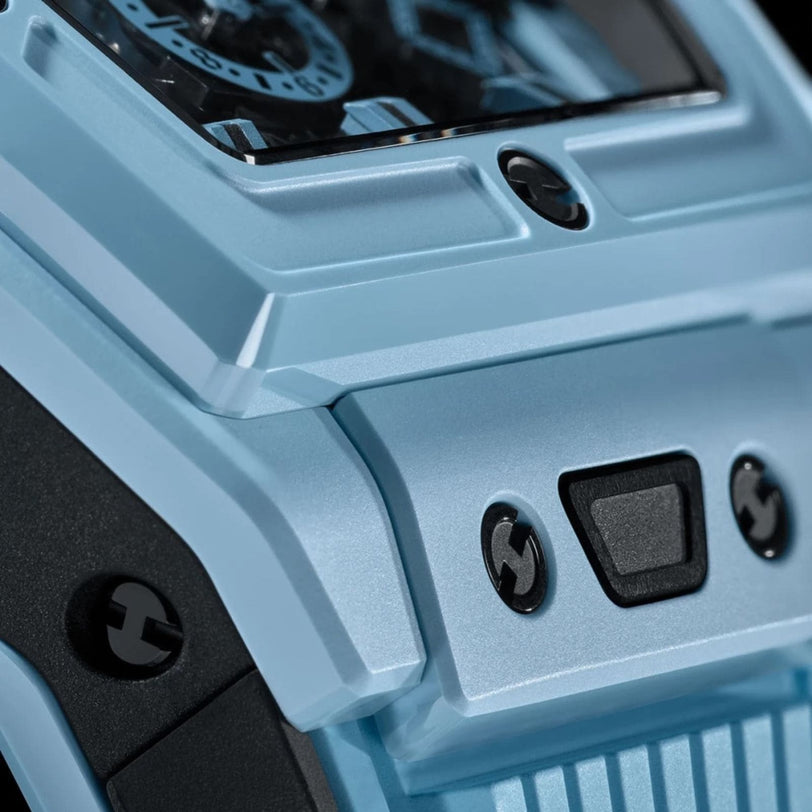Close-up of the Hublot Spirit of Big Bang Sky Blue Ceramic wristwatch case, featuring high-tech ceramic in blue, part of the dial, textured surface, and three screws above a black rubber or plastic button.