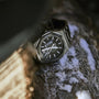 The Girard-Perregaux Laureato 42, featuring a black textured dial and silver octagonal bezel, rests on a rough, snow-dusted tree branch in natural light.