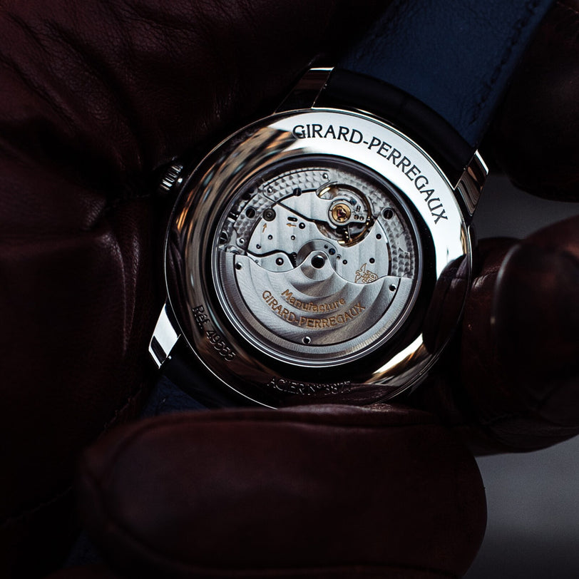 A gloved hand holds the Girard-Perregaux 1966 40 wristwatch, displaying the calibre GP0330 movement and engraved brand name through its stainless steel case back.