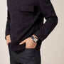 A person wears a dark button-up shirt, dark jeans, and a Cartier Santos de Cartier Chronograph watch with hands partially in pockets.