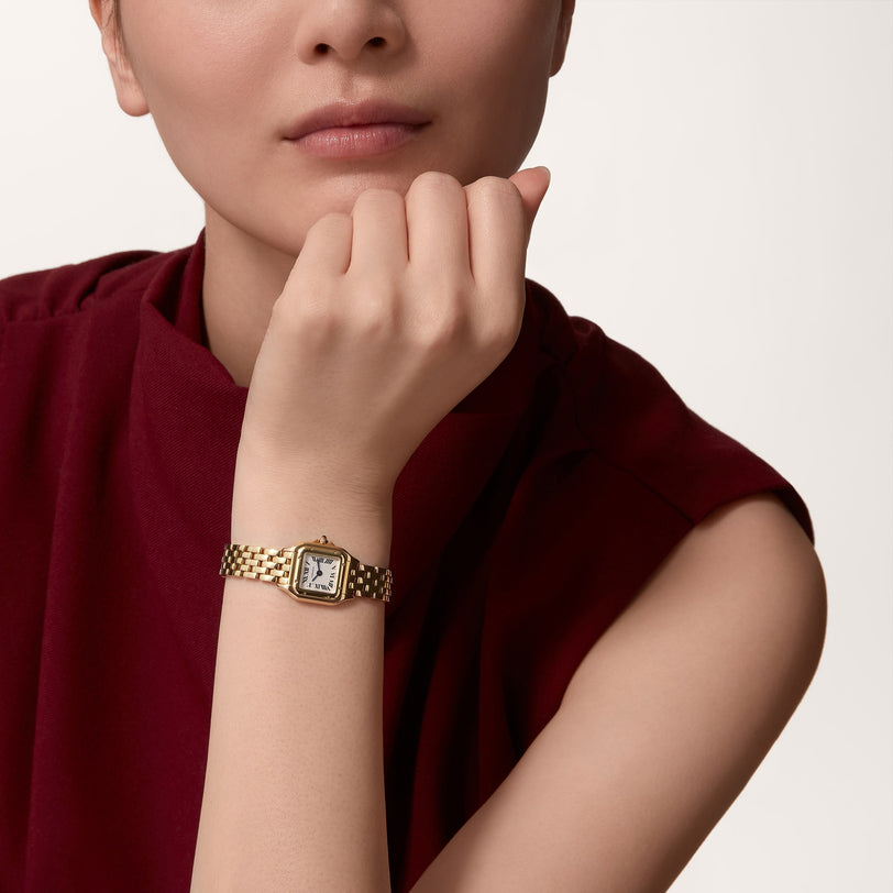 A woman wearing a sleeveless maroon top rests her chin on her hand, showcasing the elegant Panthère de Cartier gold wristwatch by Cartier.