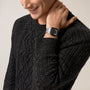A man smiles and touches his neck while wearing a dark cable knit sweater and a Cartier Santos de Cartier automatic watch.