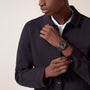 A person in a dark jacket adjusts their sleeve, showcasing the square black Santos de Cartier watch by Cartier against a plain background.