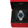 The Ballon Bleu de Cartier watch features a steel bracelet, blue dial with Roman numerals, and is shown in an open red Cartier box with a black interior.