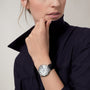 A person in a dark blazer holds their collar, showcasing the Cartier Ballon Bleu de Cartier with Roman numerals, a round silver case, and a black alligator leather strap.